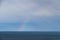 A faint rainbow arching over the vast Pacific Ocean