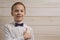 A fair-haired boy of 10 years in a white shirt with the self-tie bow tie smiles against the background of a wooden wall. Like