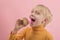 Fair-haired boy eats cupcake with pink icing. Grinning child wants to bite off piece of muffin. Side view