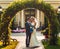 fair-haired bride with a bouquet of flowers in her hands and her fiance are standing near a natural arch