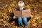 Fair haired cute boy sitting in autumn Park and reading book. Child in woods with big book in hands