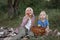 Fair-haired cute siblings sit in meadow on bedspread with apples in hand. Picnic for children on warm summer day