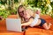 Fair-haired one year old female kid looking at a laptop cartoon with mother blonde freelancer surfer on sunbeds resort
