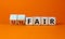 Fair or unfair symbol. Turned a cube and changes words `unfair` to `fair`. Beautiful orange background. Business and fair or