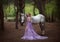 A fairy in a purple, transparent dress with a long train - caught a unicorn. Fantastic magical, radiant horse. Blonde