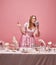 Fairy tale blond princess wearing renaissance dress standing near the laid festive table with ice cream over pink studio