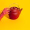 Fake hand holding clay teapot on yellow background. Minimal stilll life isometric art