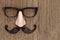 Fake mustache, nose and eyeglasses on a wooden surface