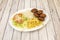 Falafel menu with balls, white rice, french fries, lettuce salad and tomato slices with white onion strips on light wooden