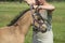 A falcon color foal in the field, wearing a fly mask, young woman takes off the fly mask