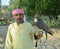 Falcon male indian senior handler in arabic national clothes with hooded falcon on his hand