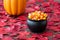 Fall color in red maple leaves on a rustic wood floor with a black cauldron filled with holiday candy corn, with pumpkin in backgr