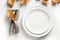 Fall table setting with autumn leaves and white plate on white table. Space for design