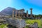 Fallen broken pillar laying on ground in front of the ruins of the Temple of Apollo at Corith Greece with the acropolis of Acroco