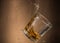 Falling glass with whiskey and spray on a brown background
