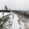 Falling snow on a hillside path with stone all and distant tree