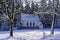 Falling snow from trees in sunlight with chapel at forest