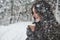 Falling snow in the woods. Girl in warm clothes with cup of coffee have a walk in the winter forest