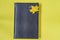False reptile leather notebook of black color with maple leaf as bookmark on yellow background
