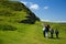 Familiy is hiking, mother and three kids walks along a green grass covered irish land.