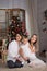 A family with a baby sits sitting near the Christmas tree