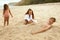 Family On Beach. Mother Burying Son In Sand And Laughing. Little Girl Standing Near Young Woman And Boy.