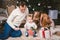 Family celebratory Christmas evening. Family three Caucasian people sitting under coniferous tree Christmas tree on floor of carpe