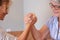 Family challenge, curly blonde daughter and senior mother joking arm wrestling on the table at home face to face