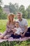 family with a child a boy of 4 years old with a car toy sitting on a green field under a tree in summer on a blanket.