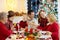 Family with children eating Christmas dinner at fireplace and decorated Xmas tree. Parents, grandparents and kids at festive meal