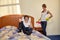 Family conflict. Young wife cleaning  room quarrels with the husband lying on a bed