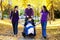 Family with disabled child in wheelchair walking among autumn le