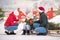 Family drinking tea to keep warm on a sleigh with a Christmas tree in a snowy winter outside