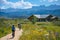 A family enjoys a bike ride on a scenic trail surrounded by wildflowers, with majestic mountains and a rustic cabin in the