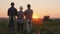 A family of farmers after work day admire the sunset over their field.