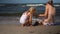 Family girls daughter and mom in swimsuits build wet sand castle on sea shore