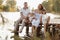 Family group active having fun by the lake. Young mother, father and two cute child daughter girls sitting on wooden