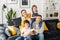 Family harmony. Happy multiracial family of four sitting on the sofa in cozy living room, looking at the camera and