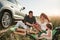 Family have picnic at countryside near silver automobile at sunset