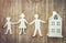 Family and home concept. Paper father, mother and son holding hands near miniature house on wooden background.