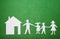 Family and home concept. Parents and children holding hands. Paper family figures and house on green textural background