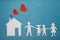 Family and home love concept. Paper house and family on blue textured background. Dad, mom, daughter and son hold hands.