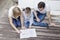 Family is kneeling on a beige carpet. In front of them is a furniture assembly manual, which they read with great care.