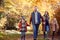 Family With Mature Parents And Two Children Holding Hands Walking Along Track In Autumn Countryside