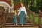 Family mom with daughter in vintage retro style linen dresses with bouquet walking dawn wooden stairs in a park garden