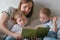 Family mom and two twin brothers toddlers read books laying on the bed. Family reading time.