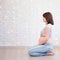 family and motherhood concept - side view of pregnant woman sitting on the floor and copy space over white brick wall