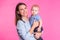 Family, motherhood, parenting, people and child care concept - happy mother holds adorable baby over pink background