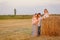 Family near haystacks on sloping field.
