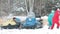 The family plays in the snow near a snowmobile in the forest